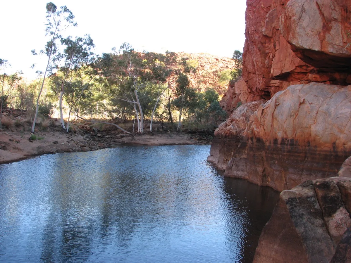 Tranquil waterhole embraced by ancient red cliffs and ghost gums
