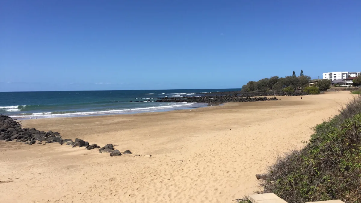 A sweep of Mackay's coastline, showing the basalt rocks, beach, and nearby town.