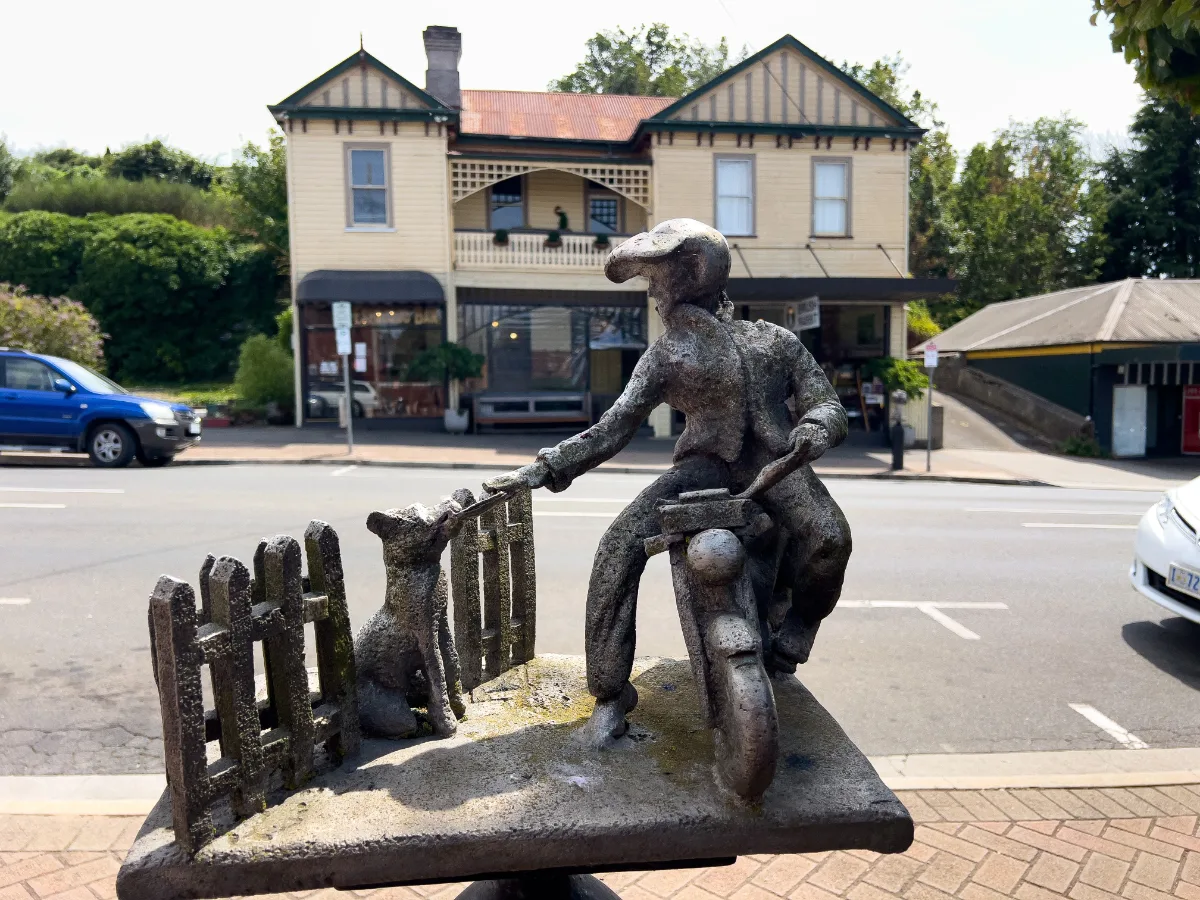 A bronze sculpture of a man on a motorbike greeting a dog, capturing a heartwarming moment.