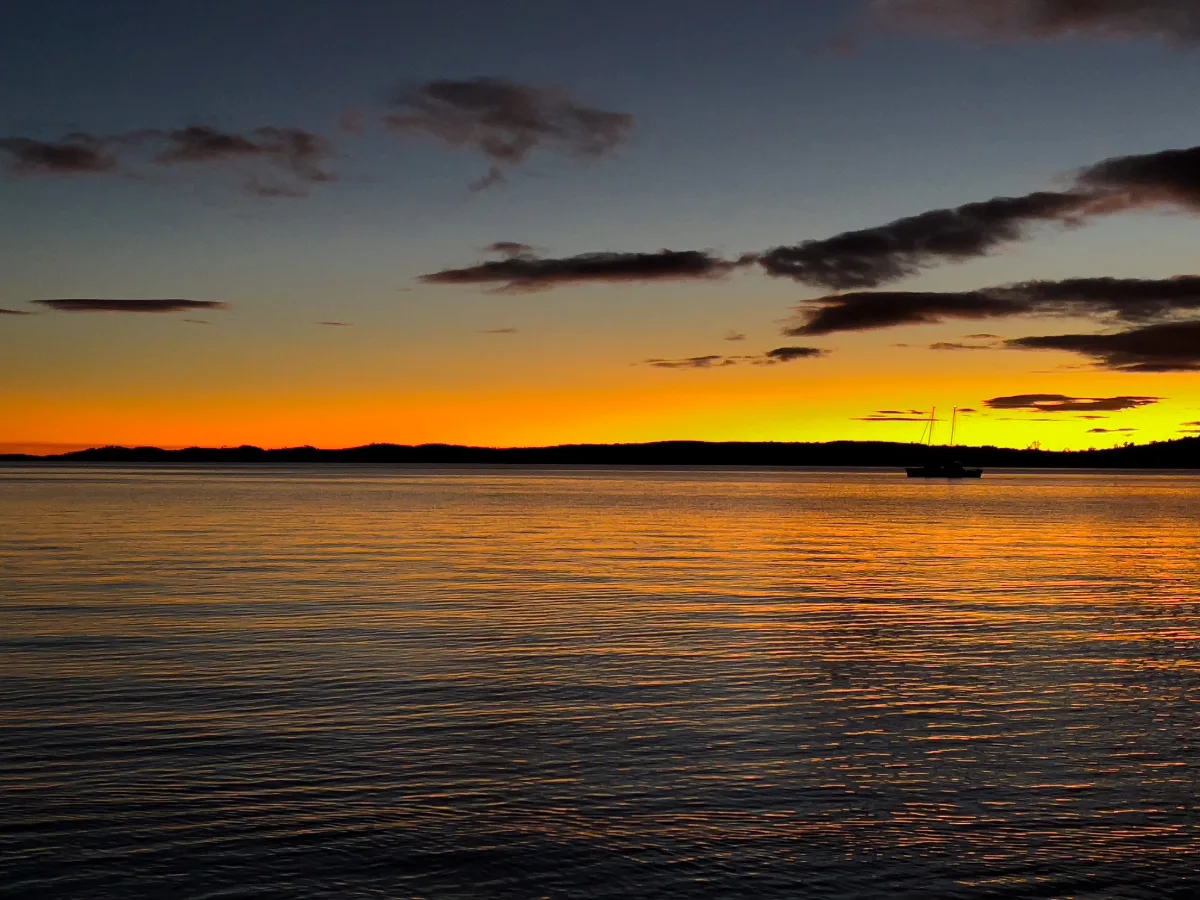A fiery orange glow breaks over the horizon at Gordon, casting a golden path across the still water.