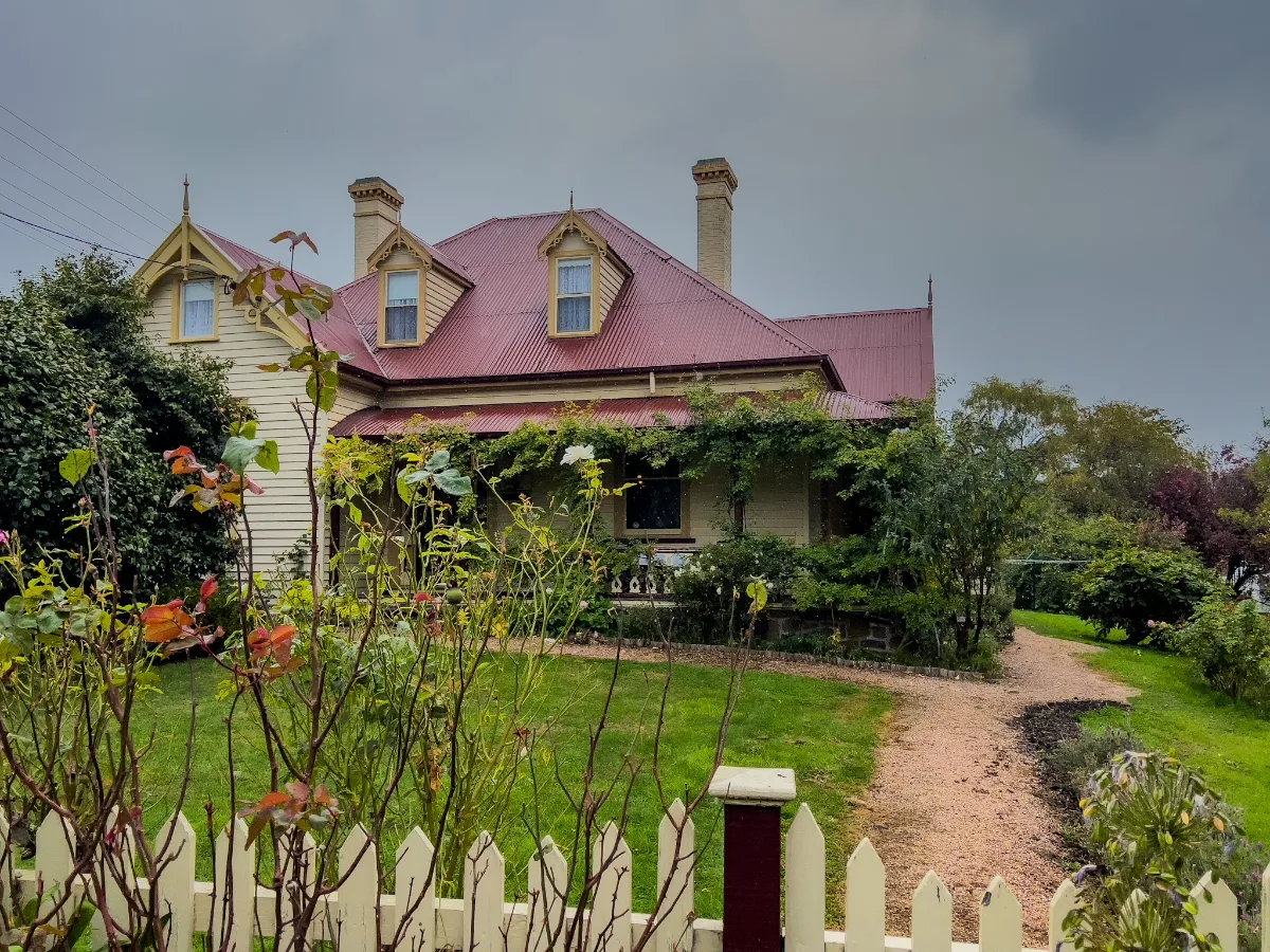 A stunning heritage home with its iconic red roof and white picket fence tucked behind the roses.