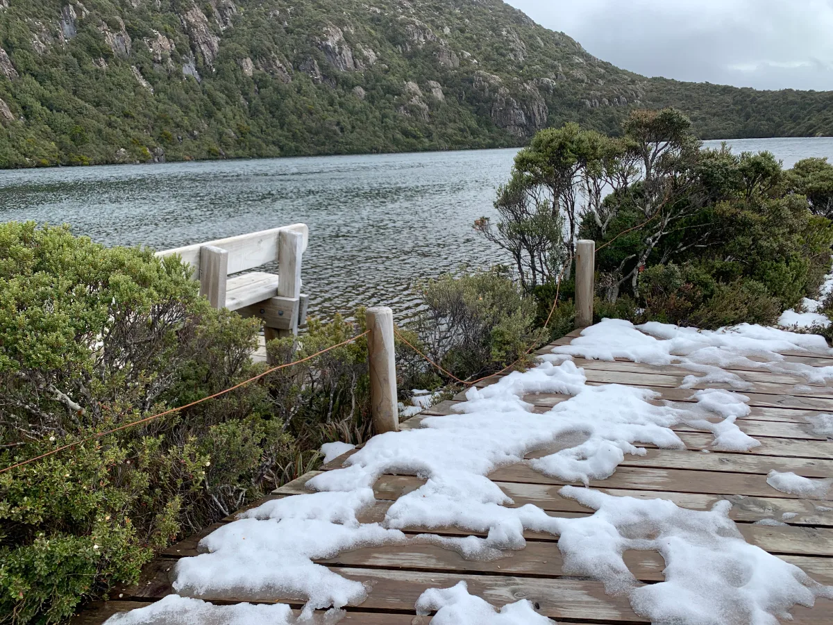 Thick patches of snow clinging to the timber walkway near the lake's edge.