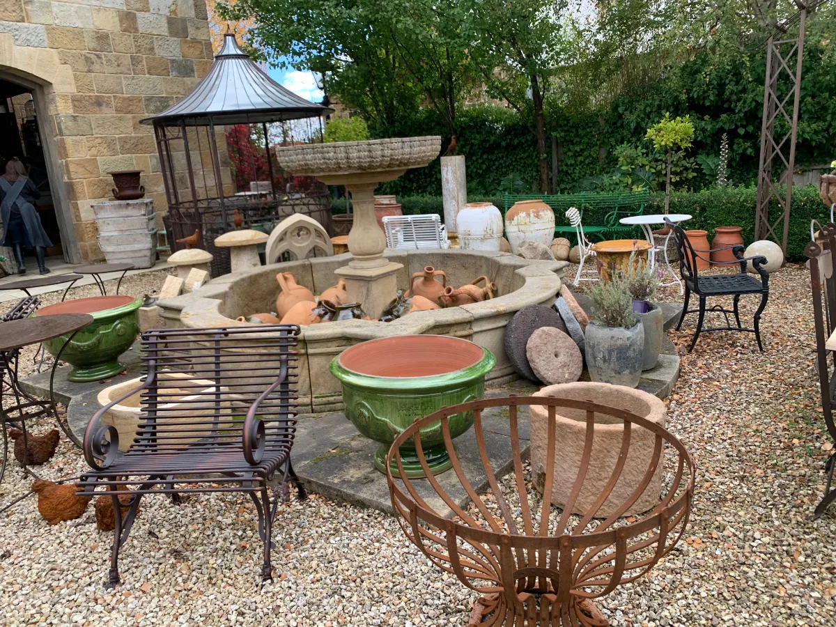 A quiet courtyard filled with rustic iron furniture, green glazed pots, and a tiered stone fountain.