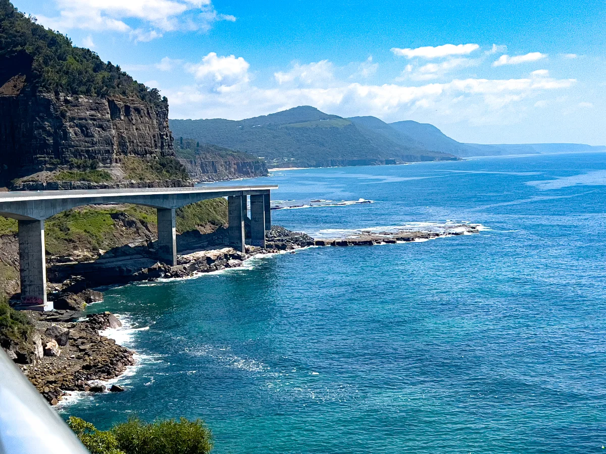 The Sea Cliff Bridge as it gracefully extends over the Pacific Ocean near Clifton, New South Wales. The cliffs serve as a magnificent backdrop.