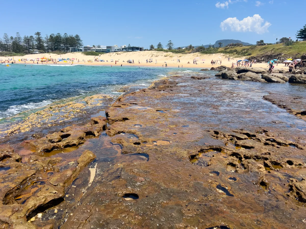 Wollongong's coastline bustles with activity on New Year's Day, offering a vibrant scene of beachgoers and stunning natural rock formations.