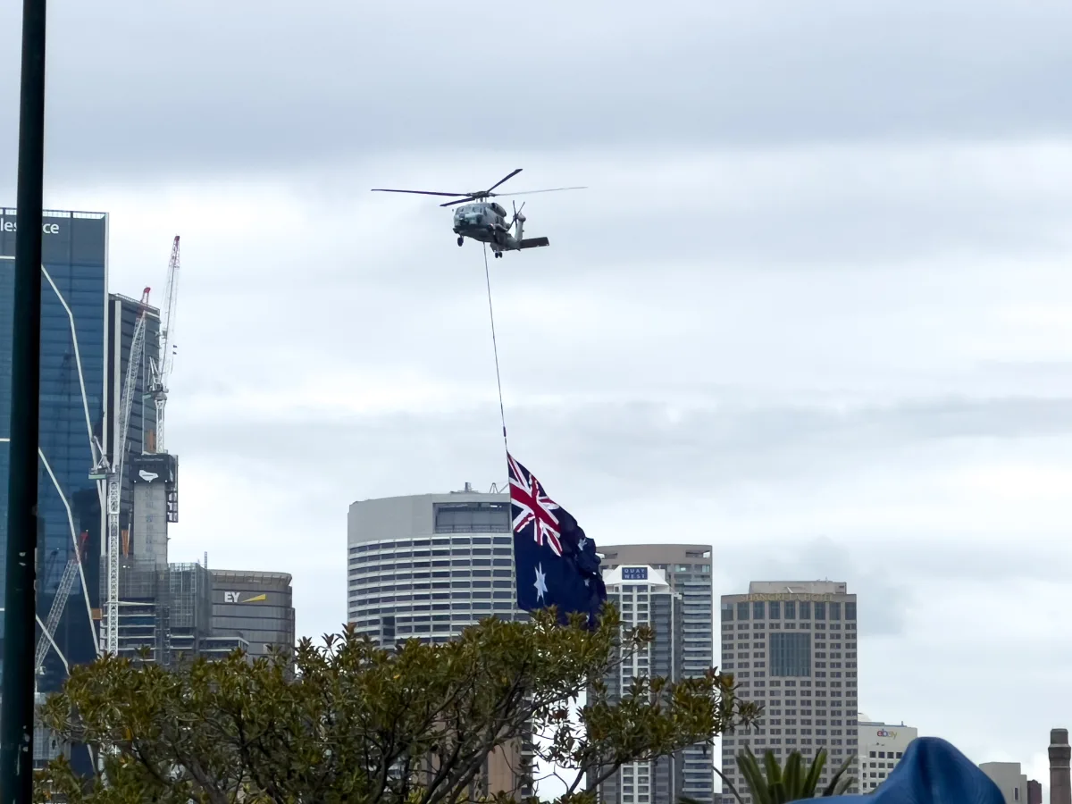 A helicopter carrying a giant Australian flag over the city skyline.