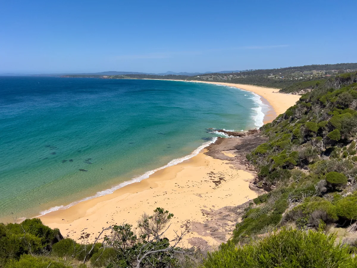 A panoramic view of Tura Beach shows its expansive, honey-colored sands and the turquoise waters beyond.