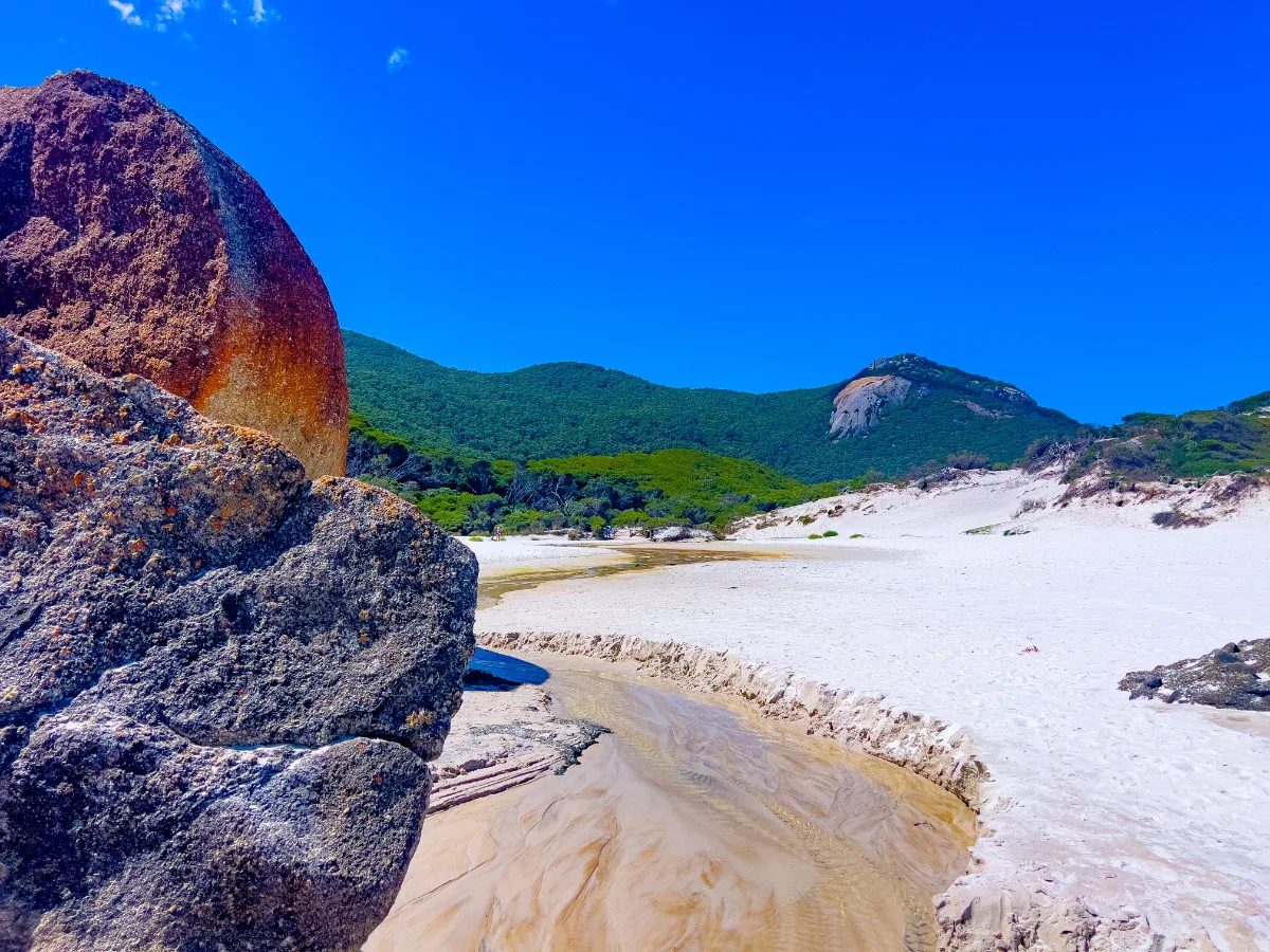 A tranquil view of Tidal River winding its way to the sea, framed by impressive rock formations.