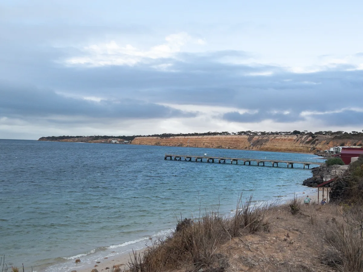The long jetty at Port Julia stretches out toward the cliffs in the distance. The water looks calm and refreshing.