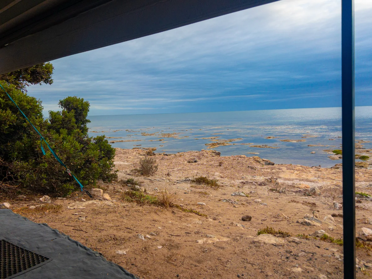 Through the window, the wide, flat coastline stretches into the sea, a rugged view from our quiet camp at Point Souttar.