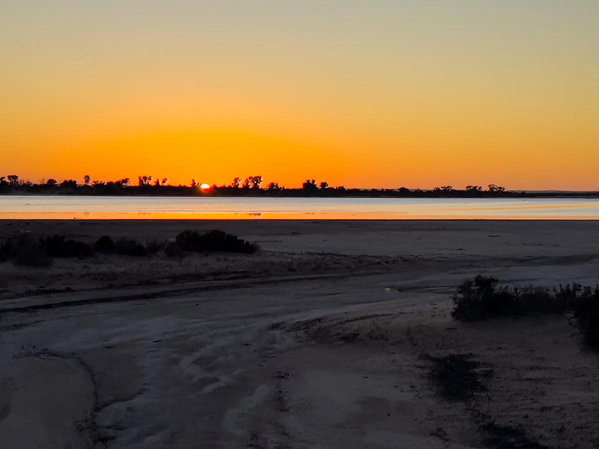 The sun dips below the horizon, painting the sky with fiery oranges and reds reflected in the lake.