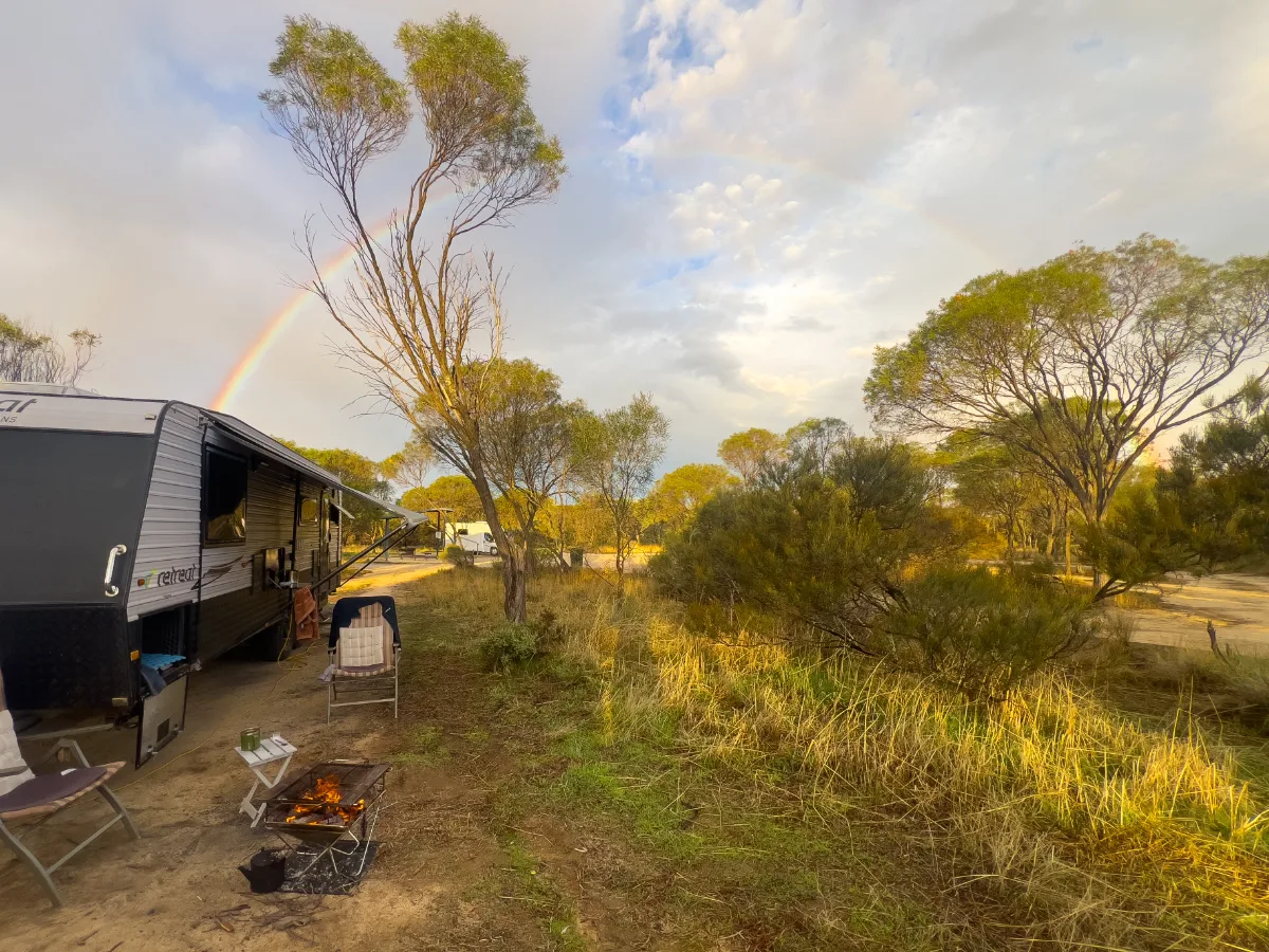 A rainbow stretches across the sky near Kwolyin, marking our last night on the road before heading back to Perth. You can see a campfire set up with our caravan to the left.
