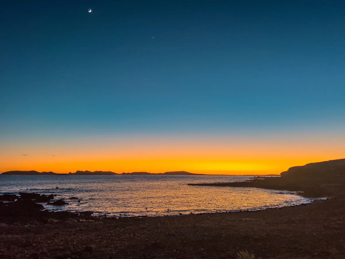 Crescent moon rises as sunset fades over coastal waters
