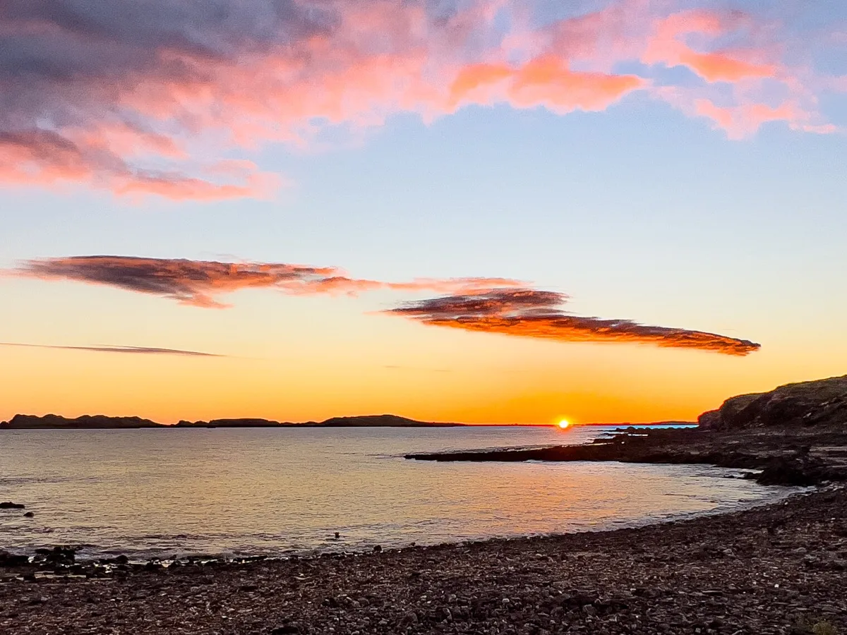 Golden sunrise over rocky coastal waters and distant islands