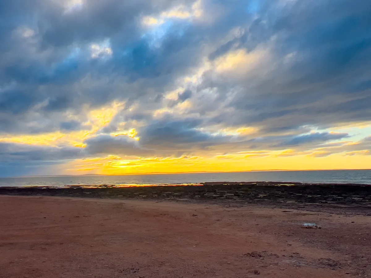 Dramatic sunset paints the sky over red earth shores
