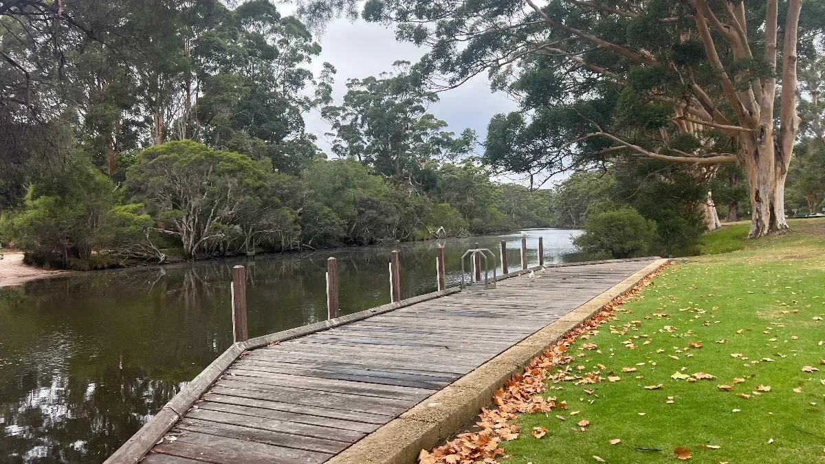 The still river reflects the surrounding trees and a landing platform.